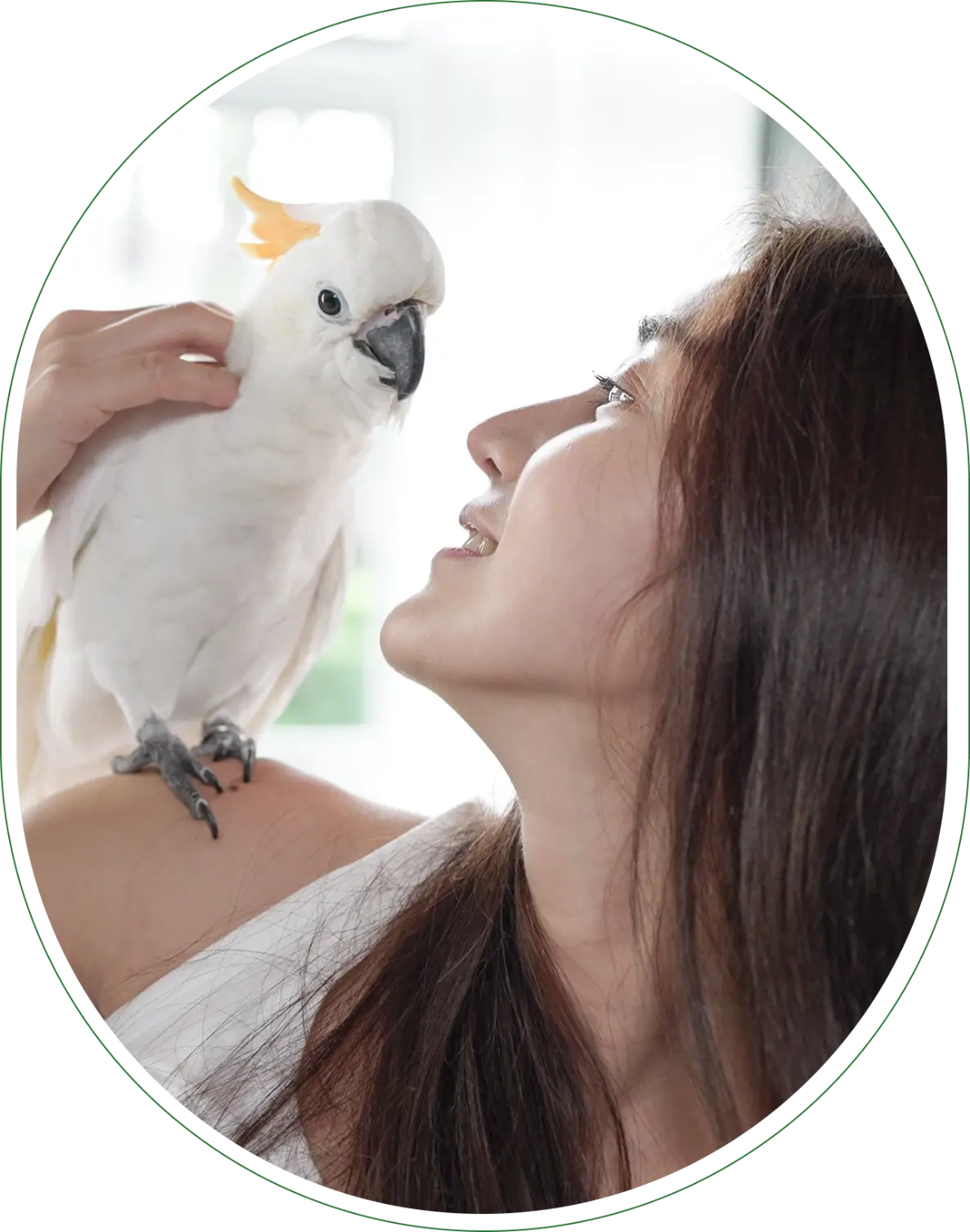 Woman smiling at a perched white cockatoo indoors.