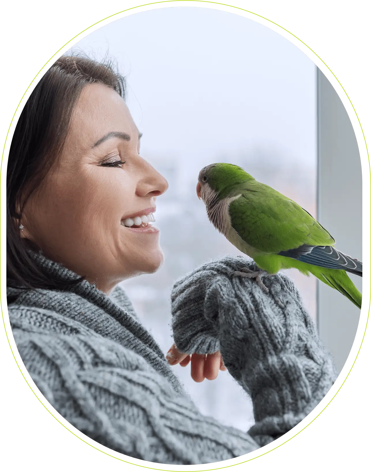 Woman smiling at green parrot indoors.
